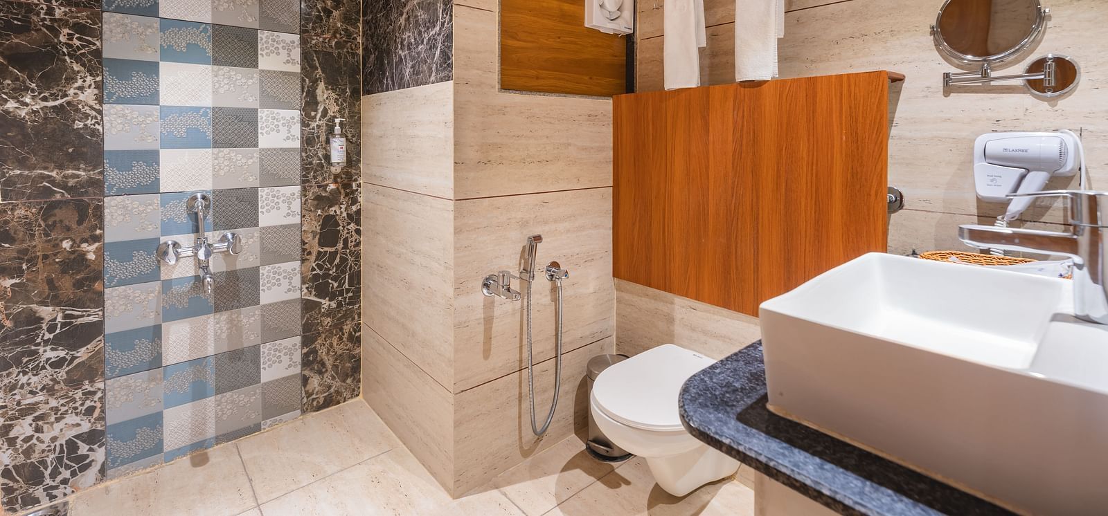 A modern bathroom is equipped with a rectangular sink, a toilet, and a shower area with patterned tiles - Lords Eco Inn Ambaji.