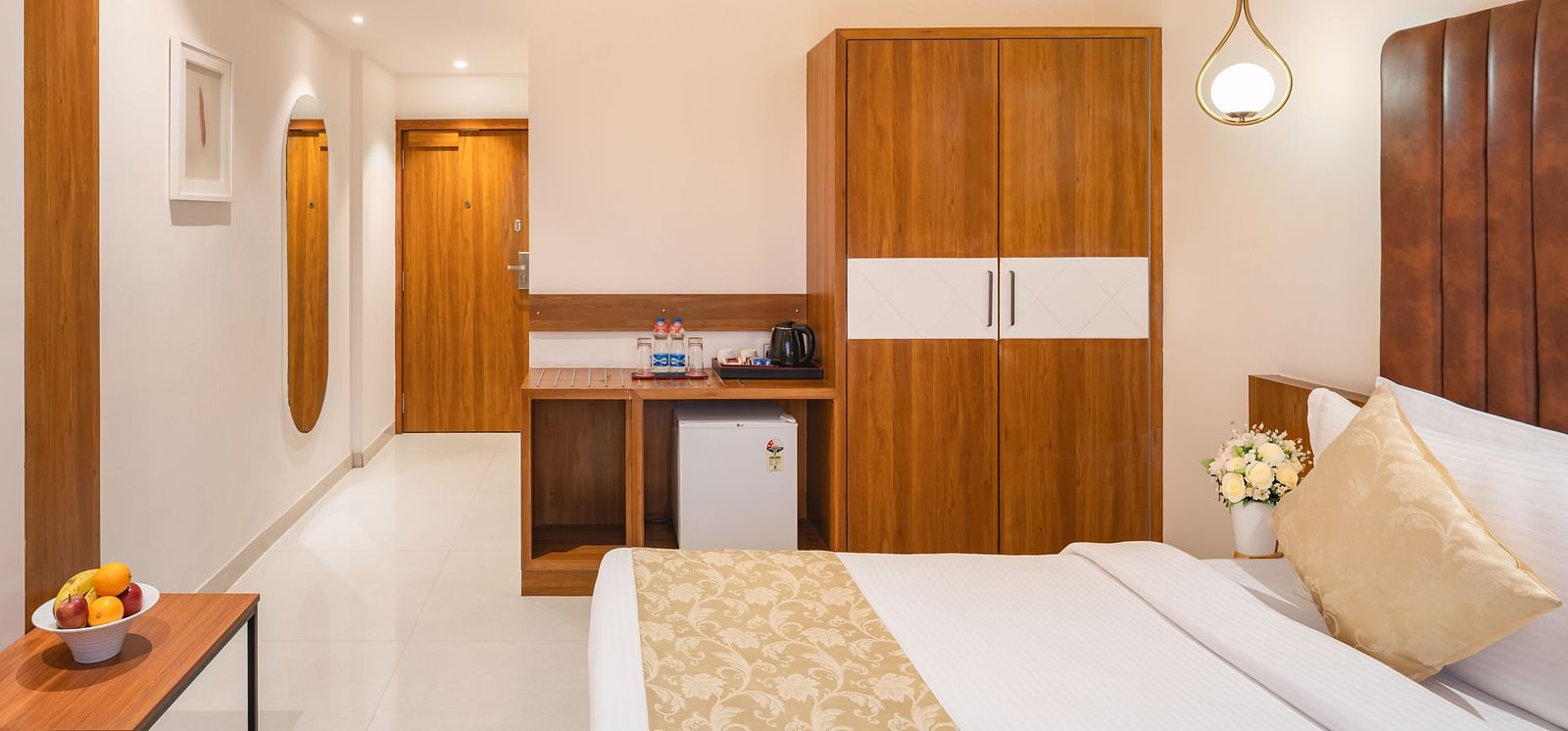 A comfortable bed with a decorative throw is featured in a hotel room with a wooden wardrobe and a desk area - Lords Eco Inn Ambaji. 