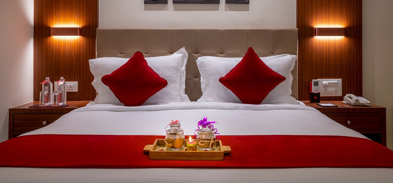 A hotel room with a bed featuring red and white bedding, artwork above the bed, and warm lighting.