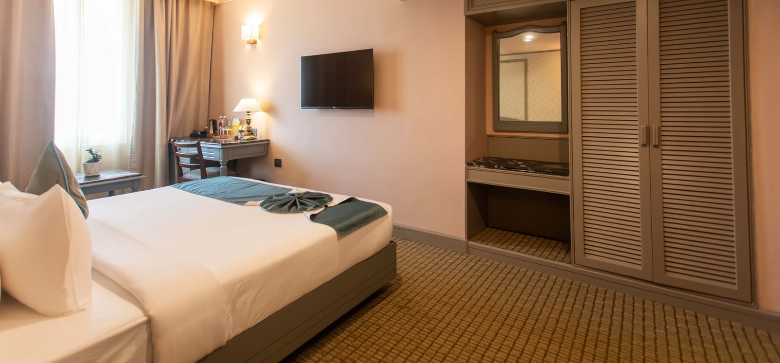  A guest room at Shilton International, Kochi, with a bed, wall-mounted television, and a built-in wardrobe.