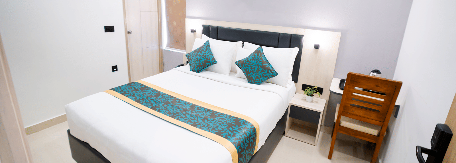 A room featuring a spacious bed, wall-mounted A/C above the headboard, a mirror, and a closed door to the side at Sunrise Business Hotel, Hyderabad.