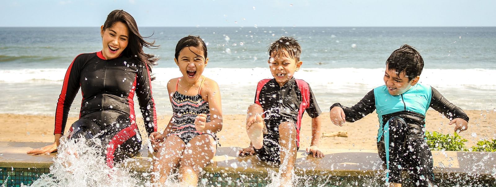 A woman and three children splashing water by a pool