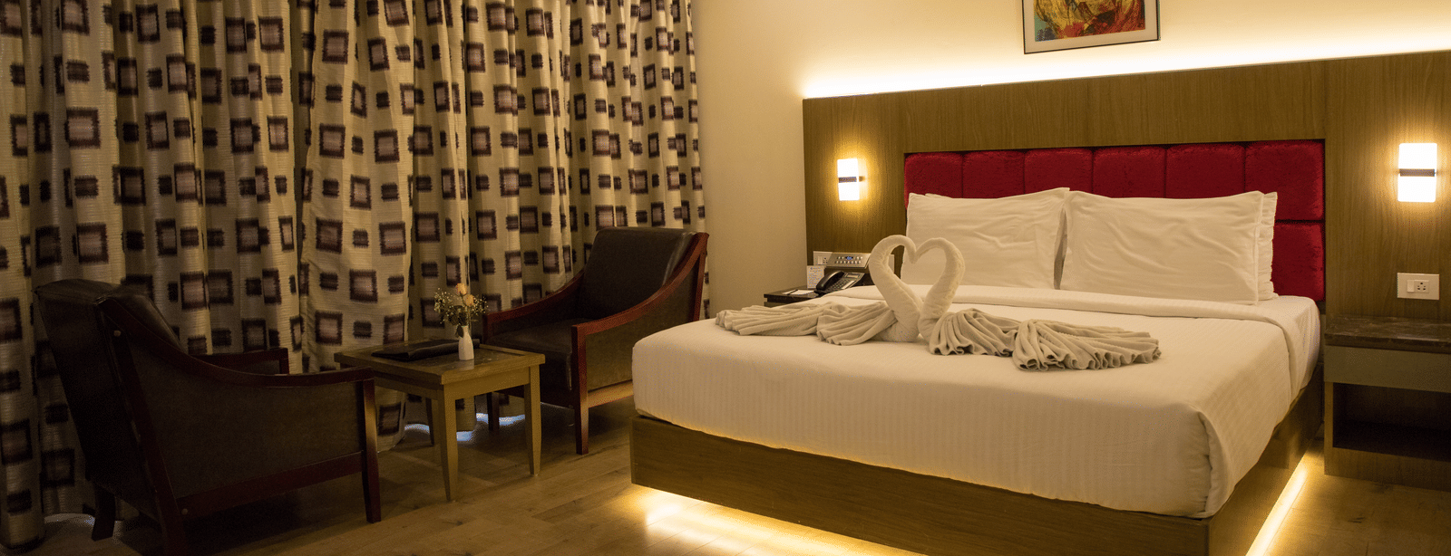 Full view of the Deluxe Room at the Benzz Park, Vellore, featuring a double bed with under-bed lights alongside a common seating area.