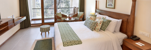 Deluxe room featuring a fluffy bed, beside table, sitting area with sofa chairs and a centre table. This room at Suryavilas Luxury Resort and Spa also has a balcony attached.