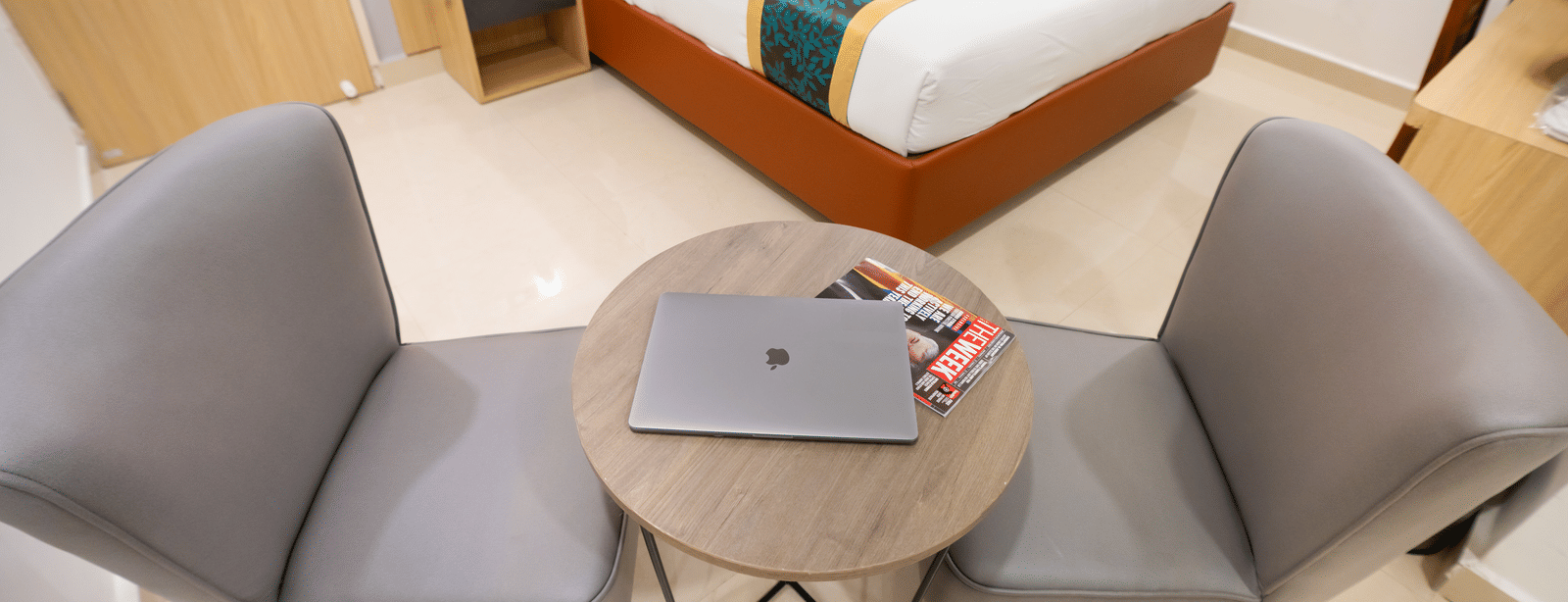 A close-up view of a small round table with a laptop and chairs on either side, with a large bed in the background at Sunrise Business Hotel, Hyderabad.