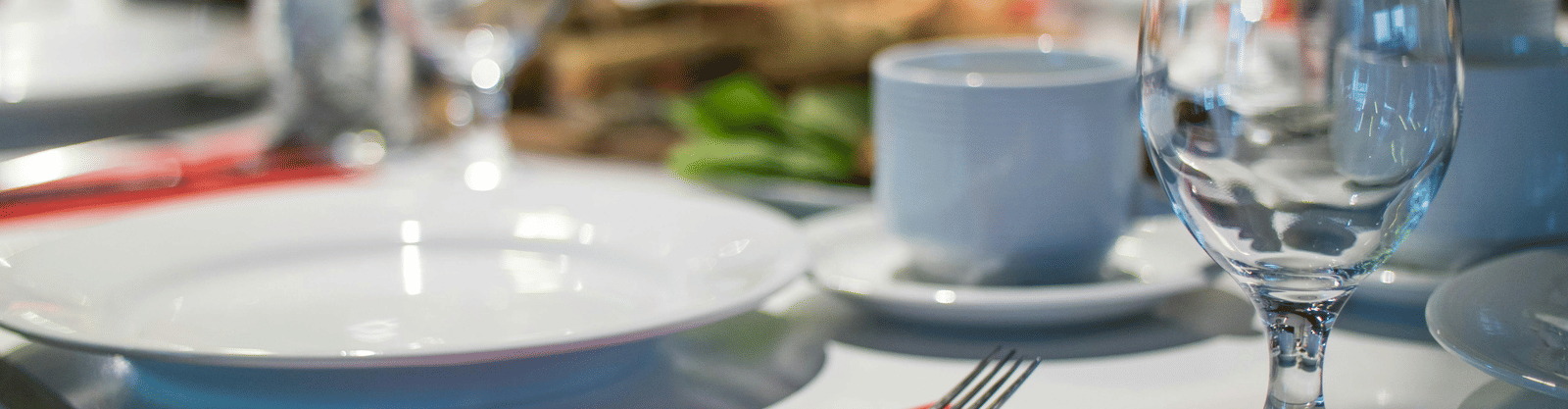 A close-up, blurred shot of a formal dinner table setting with white plates, red napkins, silverware, and clear wine glasses.