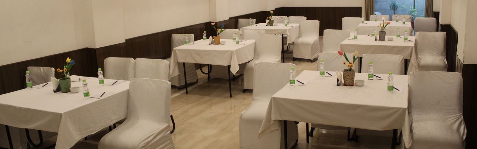 An image of a banquet hall at Inde Hotels Vista Woods featuring several sets of chairs and table where water bottles and flower pots are placed 