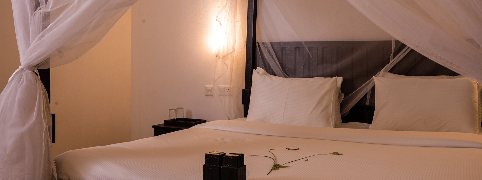 A wooden bed with a draped mosquito net and white linens in a guest room at Ayur On The Beach Nattika.