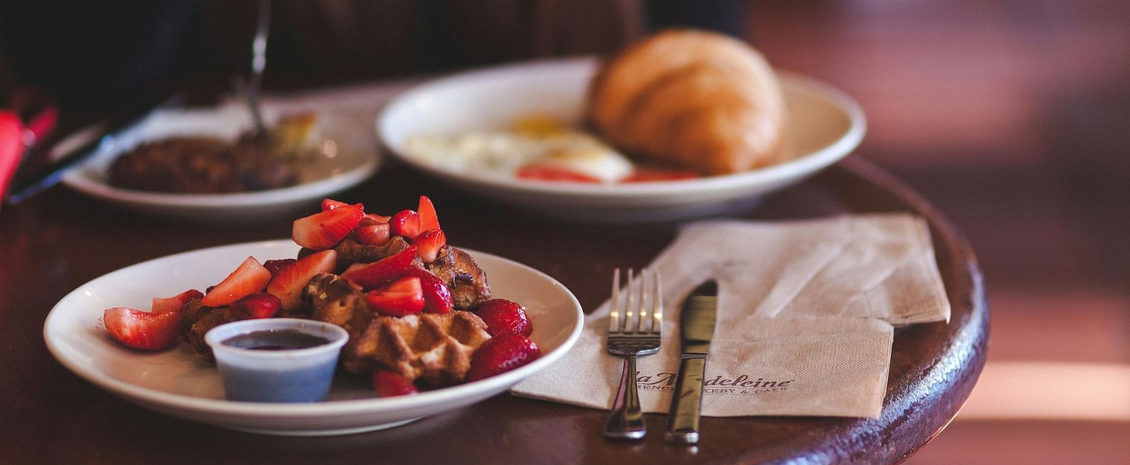 Waffle with strawberries and a croissant served on a round coffee table in a cafe. 