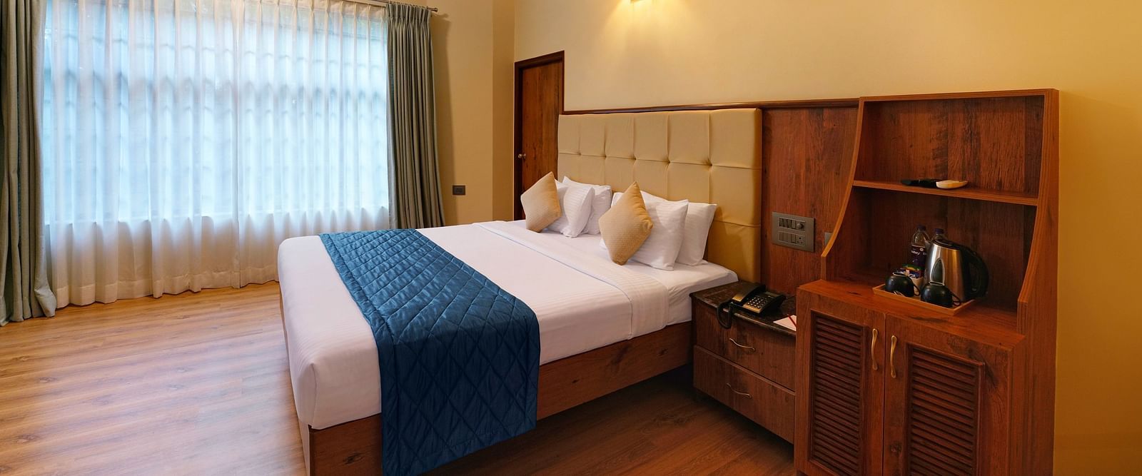 A room in bengaluru with large windows, a queen size bed, and wooden decor - Cross Roads Inn, Bengaluru