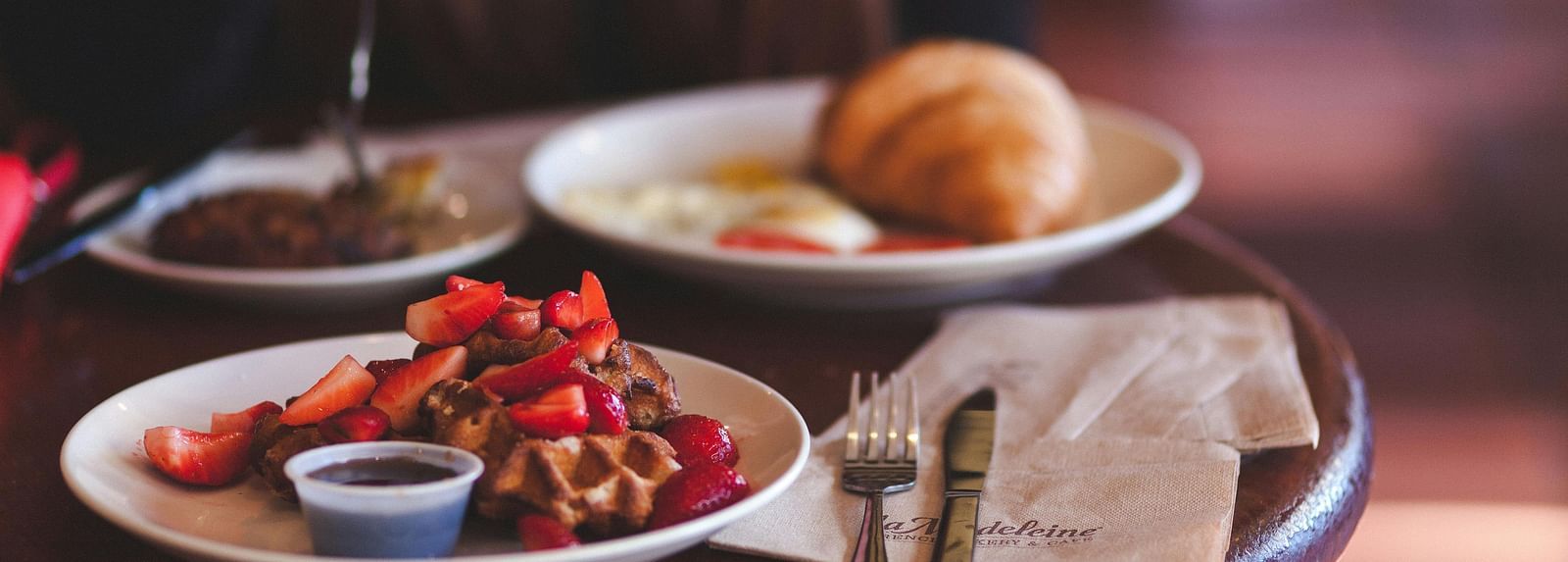 Waffle with strawberries and a croissant served on a round coffee table in a cafe. 
