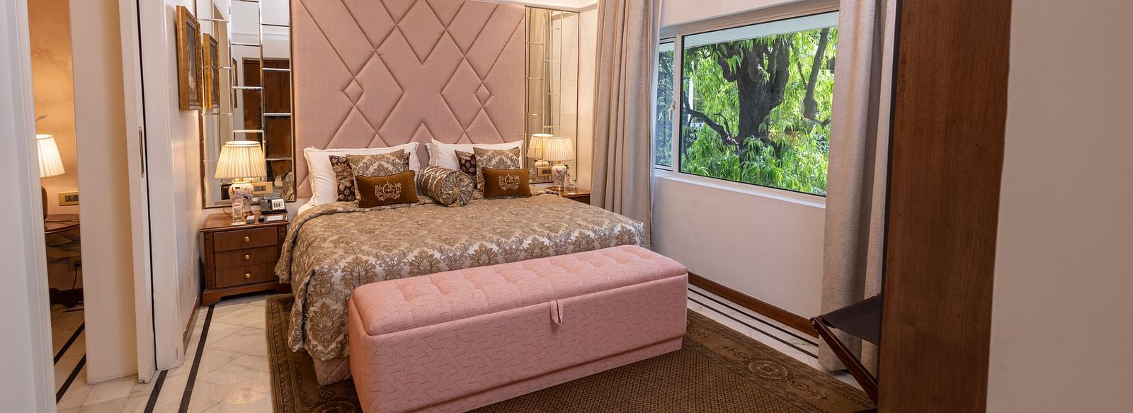 Luxury Suite at The Claridges New Delhi, featuring a cosy king sized bed with pillows and an elegant chandelier hanging overhead