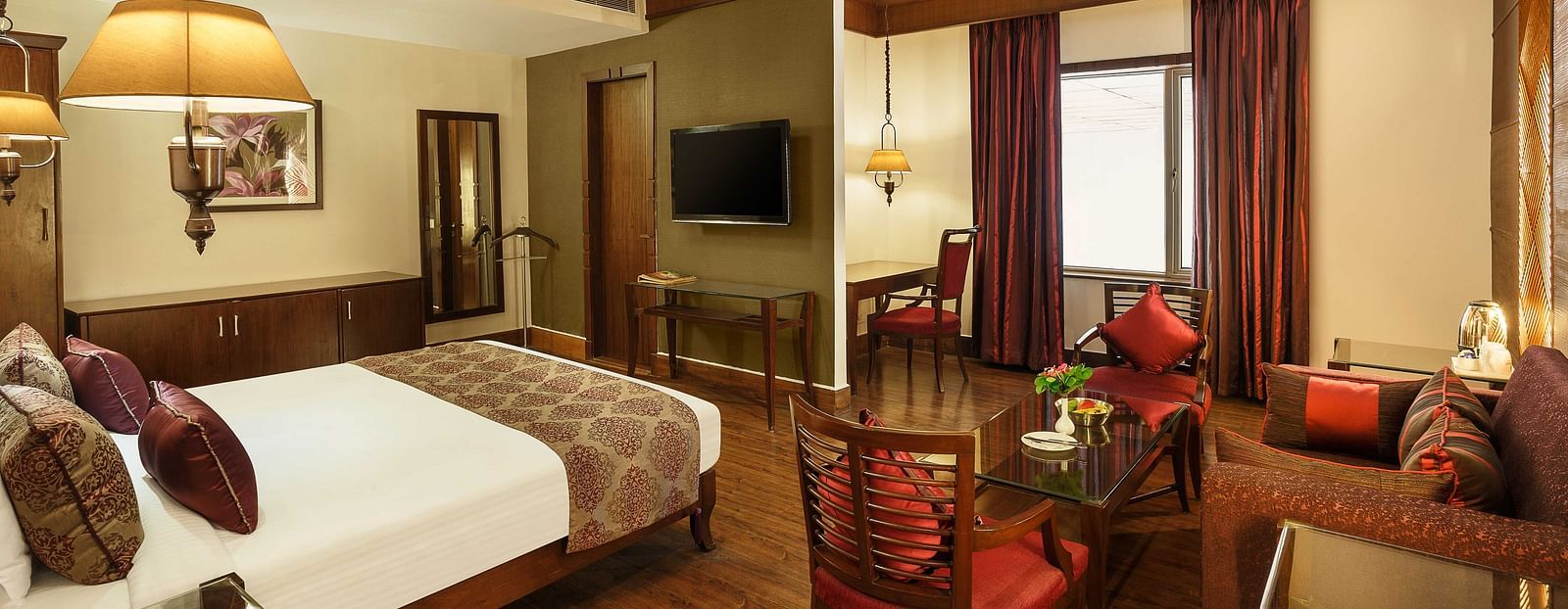 A view of a bedroom with a single bed facing a television and a desk with chairs