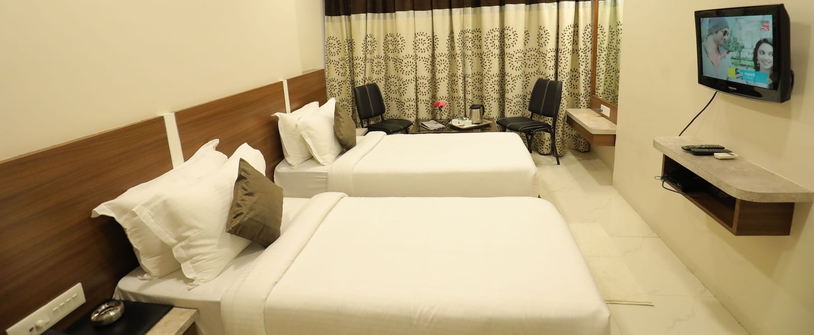 Side view of the Super Deluxe Rooms, of Highland Resort, that are furnished with twin beds, wall-mounted TV, a seating area for two, and drawn curtains.
