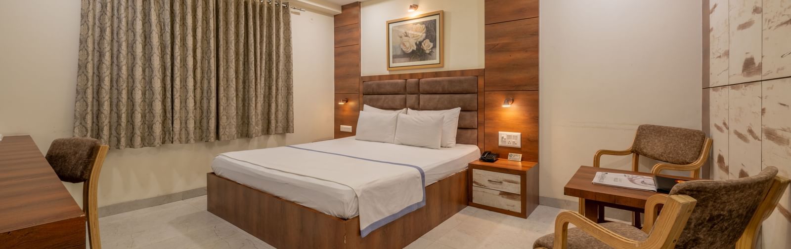 A well furnished spacious room with a king size bed, wooden furniture, and elegant curtains at Hotel Highway King, Jaipur.