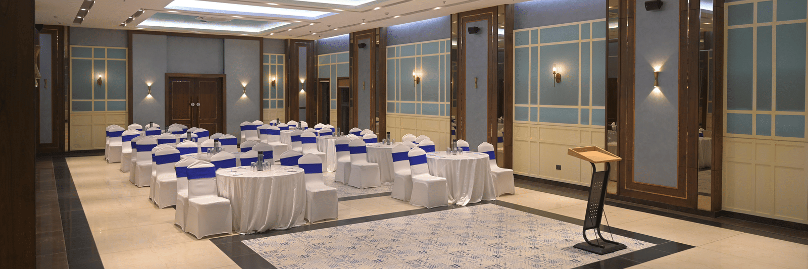 A wide view of the banquet hall featuring elegant lighting and neatly arranged seating at Hotel Sonar Bangla Mayapur.