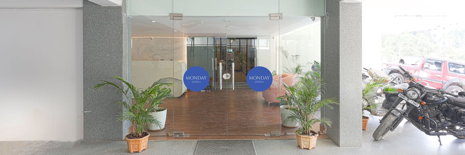 The entrance to Destino by Monday Hotels, Gachibowli, featuring transparent glass doors and potted plants.