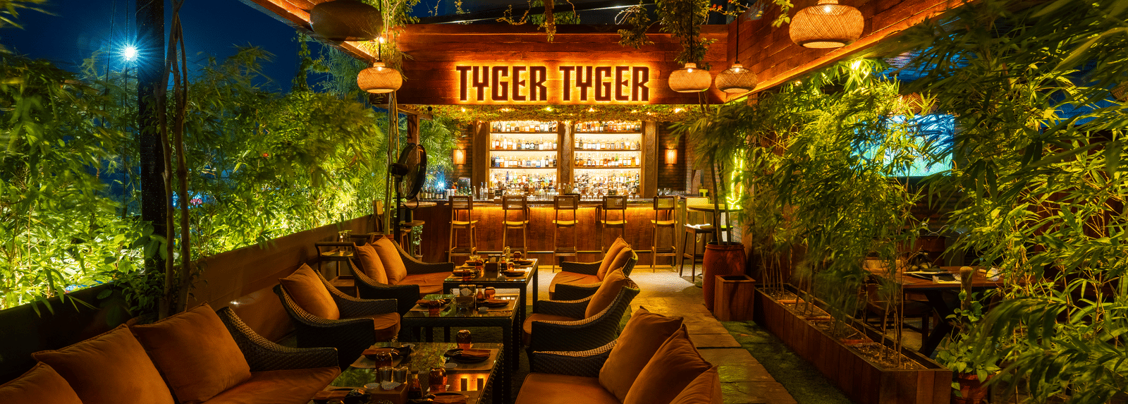 A restaurant seating area with cushioned chairs, tables and a glowing signboard reading 'TYGER TYGER' at Infiniti Hotel, Indore.