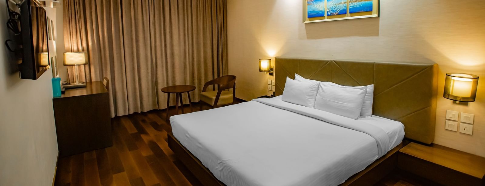 A queen bedroom with a workstation, a seating area, and bedside tables at The Hamuse Hotel, Kodaikanal