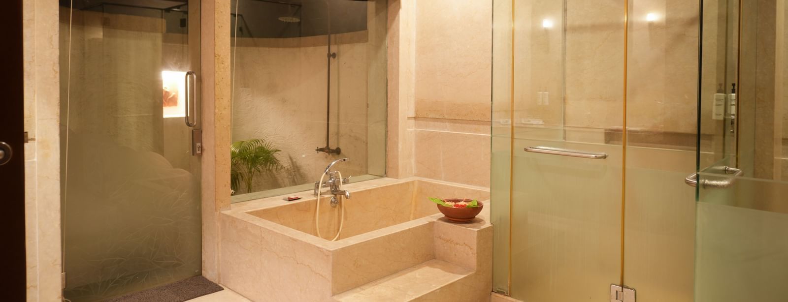 Glass-panelled shower room in the Lake View Villa at Vedic Village Spa Resort with a bathtub, shower cubicle, and a glass door opening to an outdoor shower area.