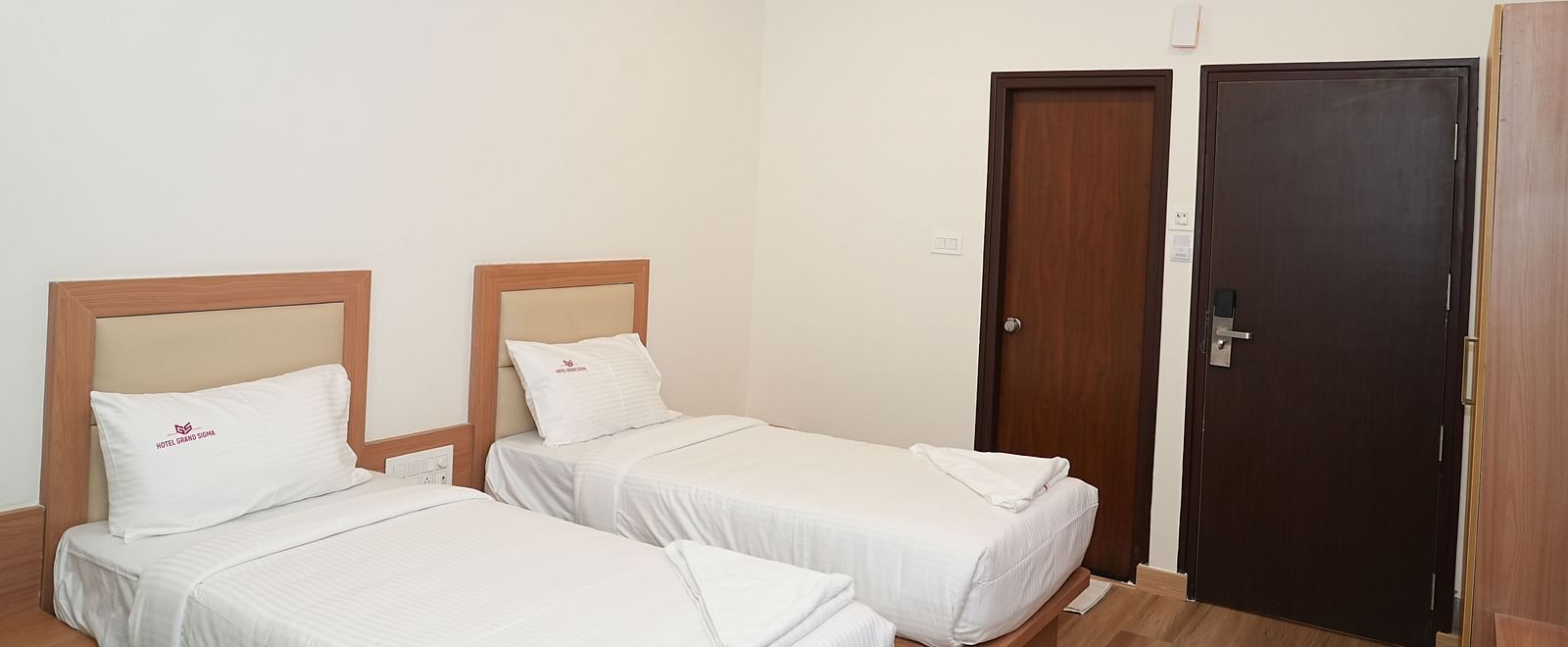 a room with two single beds along with a ceiling fan on top of thema room featuring a double bed along with a single bed with a wardrobe at the far end of the room - Hotel Grand Sigma