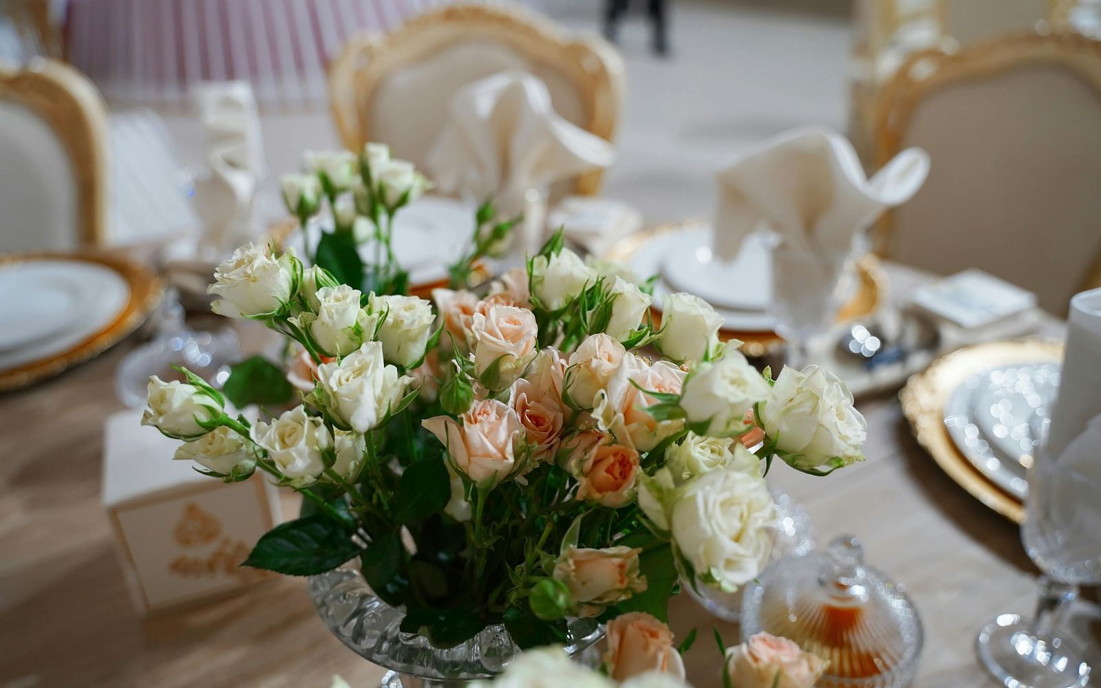 A close up shot of a beautiful flower vase with a lot of white and pink roses on a dining table.