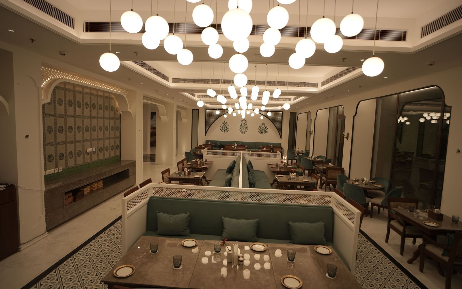 Full view shot of a restaurant with ample of warm lighting featuring well arranged dining tables along with cutlery Bhagirathi by RDB Atishay.