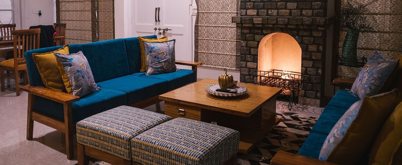 A living area with furniture arranged around a table by the fireplace at BluSalzz Villas - The Green Roof, Bhimtal.