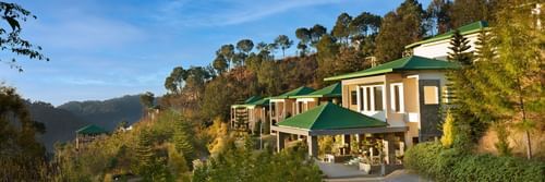 Scenic view of a hillside property surrounded by lush greenery and forested hills under a clear blue sky - Suryavilas Luxury Resort and Spa.