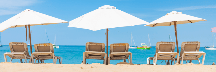 A row of empty loungers under white umbrellas lines a serene beachfront at The Soco House, facing the clear blue sky and calm ocean.