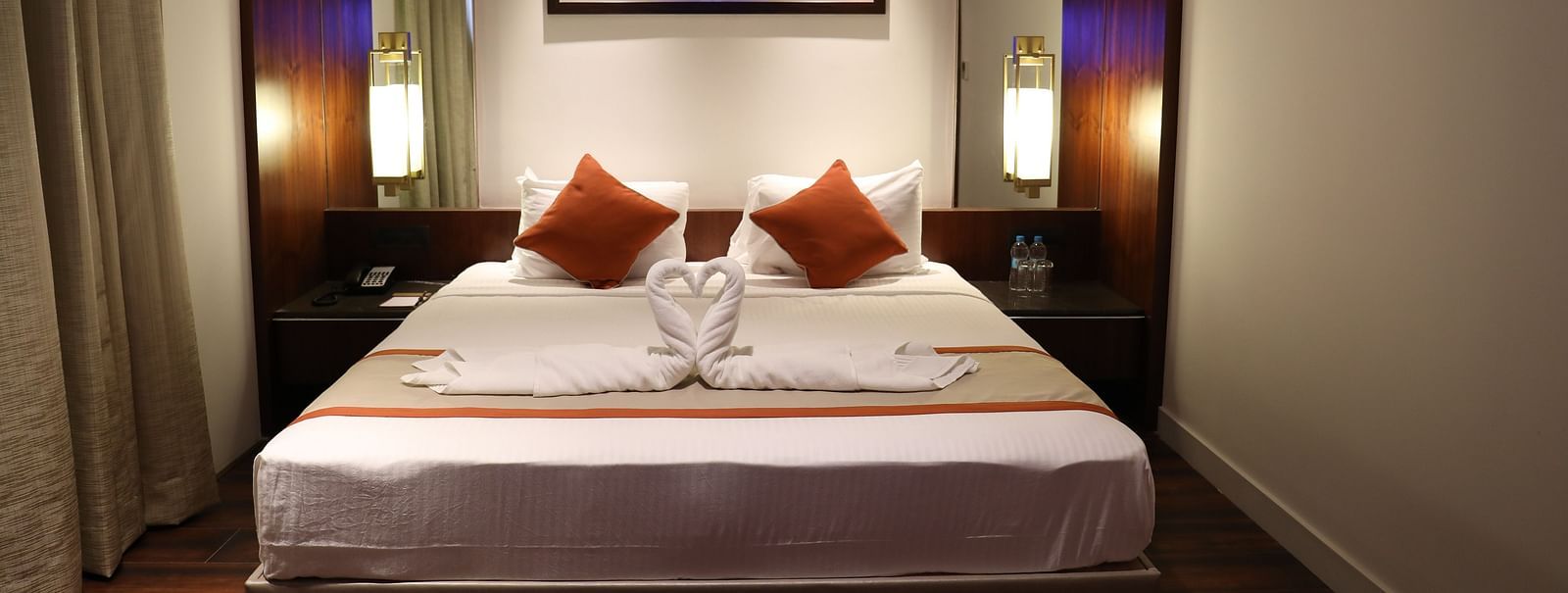 The front view of a hotel room with a large bed, white linens, burnt orange accents and a framed picture of a bridge above the headboard - Hotel Southend by TGI - Bommasandra, Bangalore