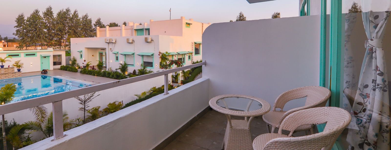A balcony at Vedikant Resorts The Mallard Corbett with chairs and a table overlooks the surroundings at dusk.