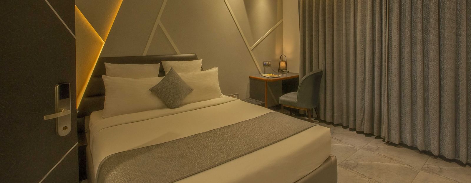 Image of well lit Coral Premium Room at Coral Reef Hotel and Spa in Port Blair featuring a plush bed and a work desk and chair next to it near the window