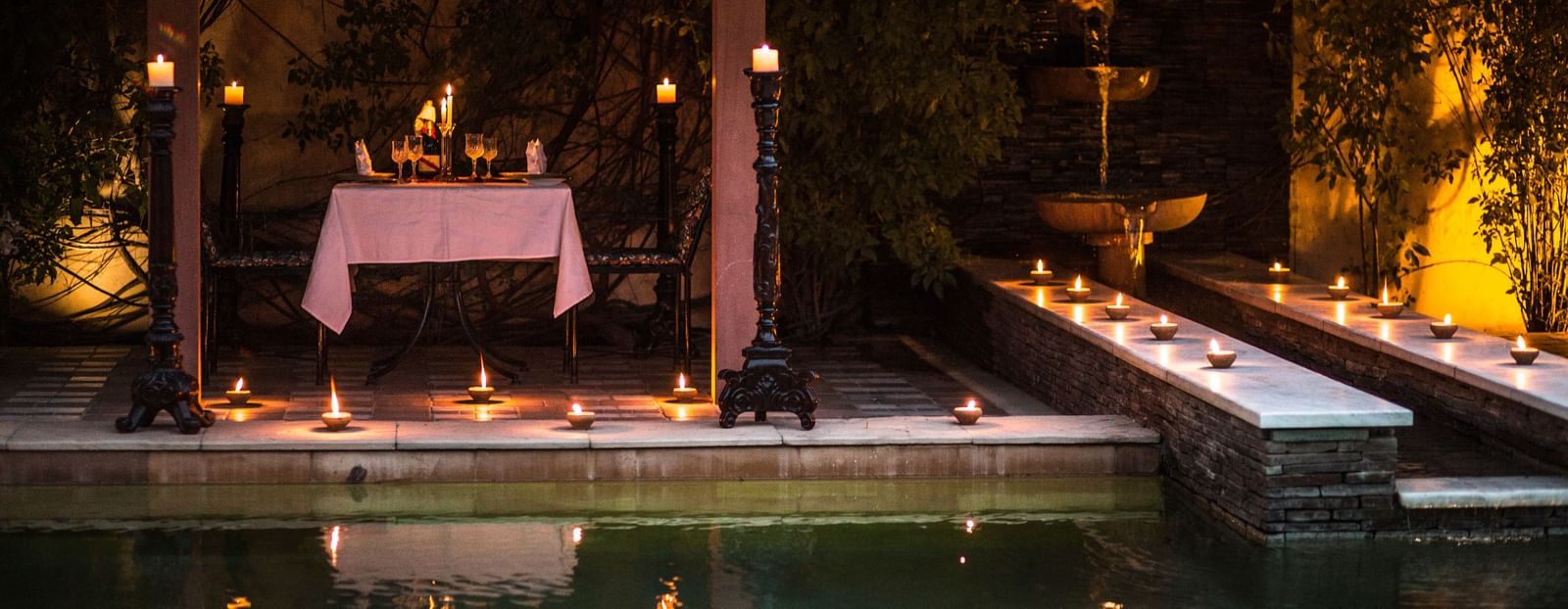View of the outdoor setup with candles and a table next to water, similar to the first image, at Royal Heritage Haveli.