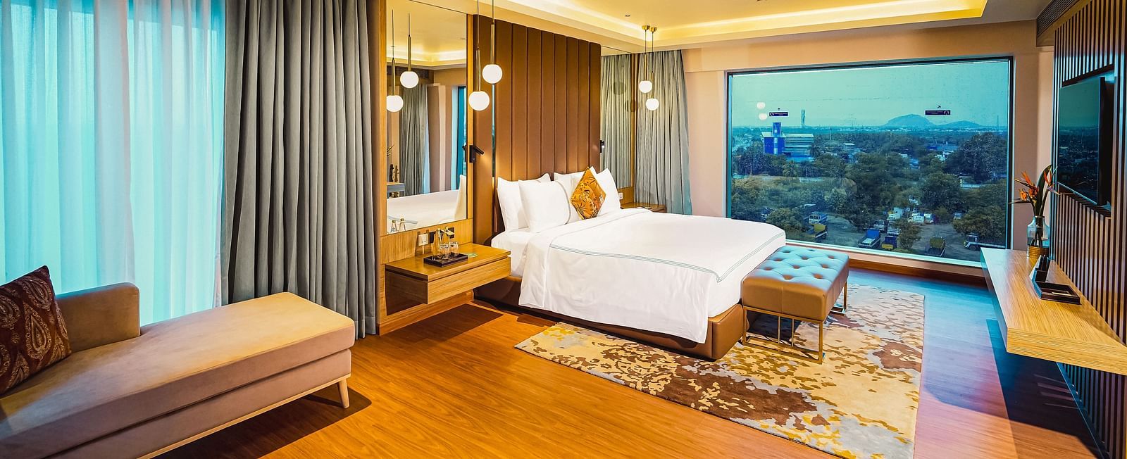 A beautiful image of a hotel room in Madurai with a large bed, a couch, and a wall-mounted television