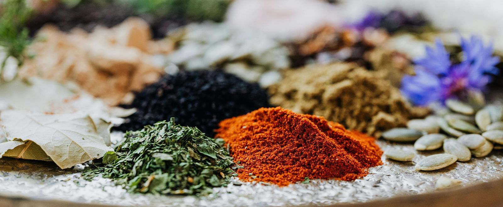  A variety of colorful spices and herbs arranged on a tray, showcasing their natural textures and vibrant colours.