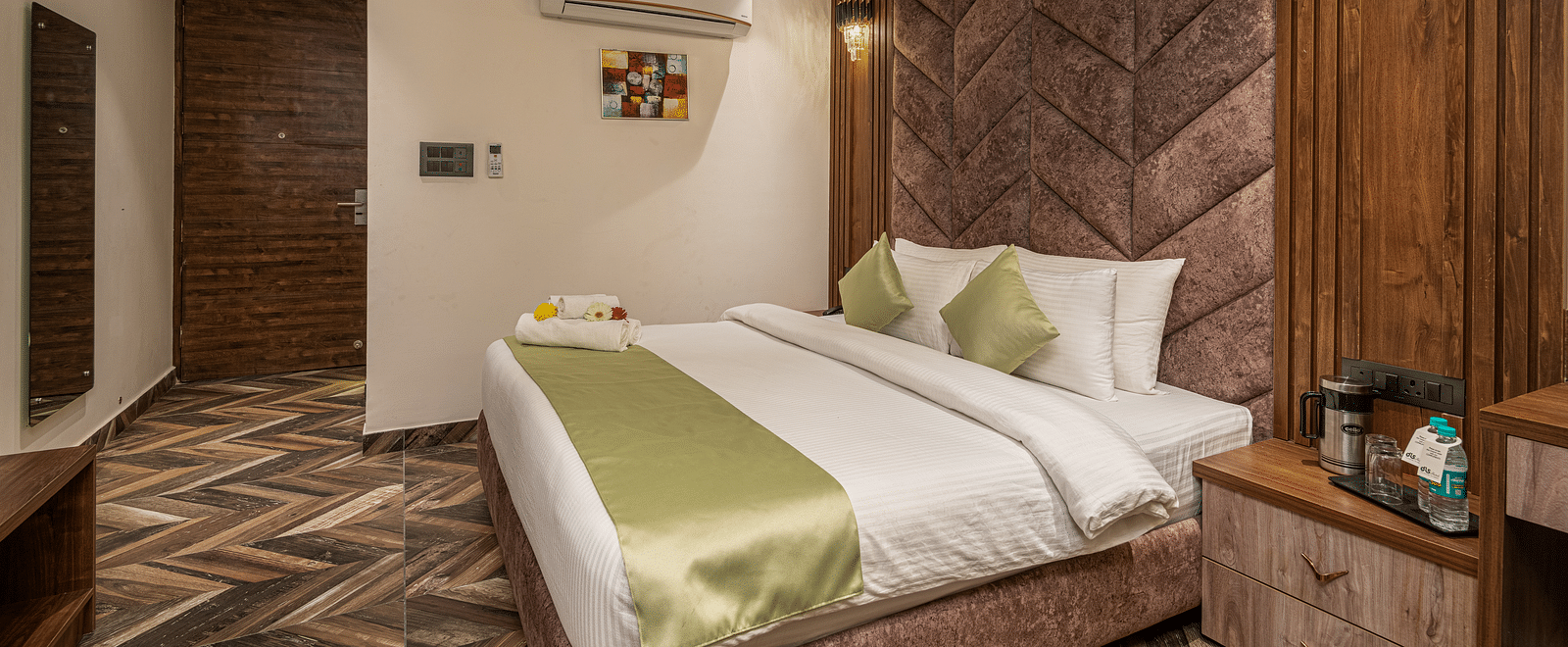 A panoramic shot of the deluxe room at DLS Grand Luxotica, Dehradun highlighting the entrance door and the double bed in the room