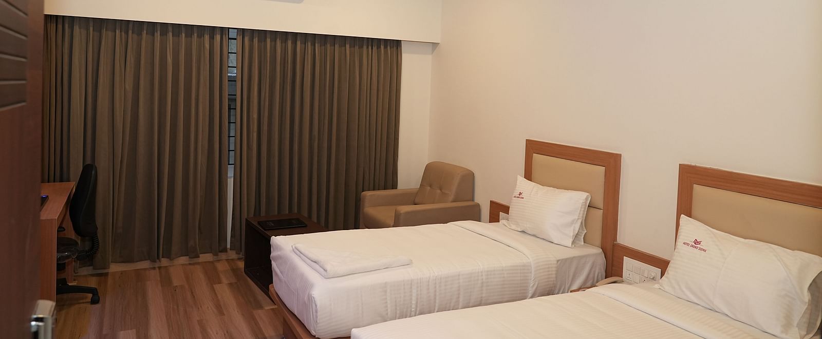 the huge windows in the bedroom covered with full length brown curtains along with a twin bed - Hotel Grand Sigma