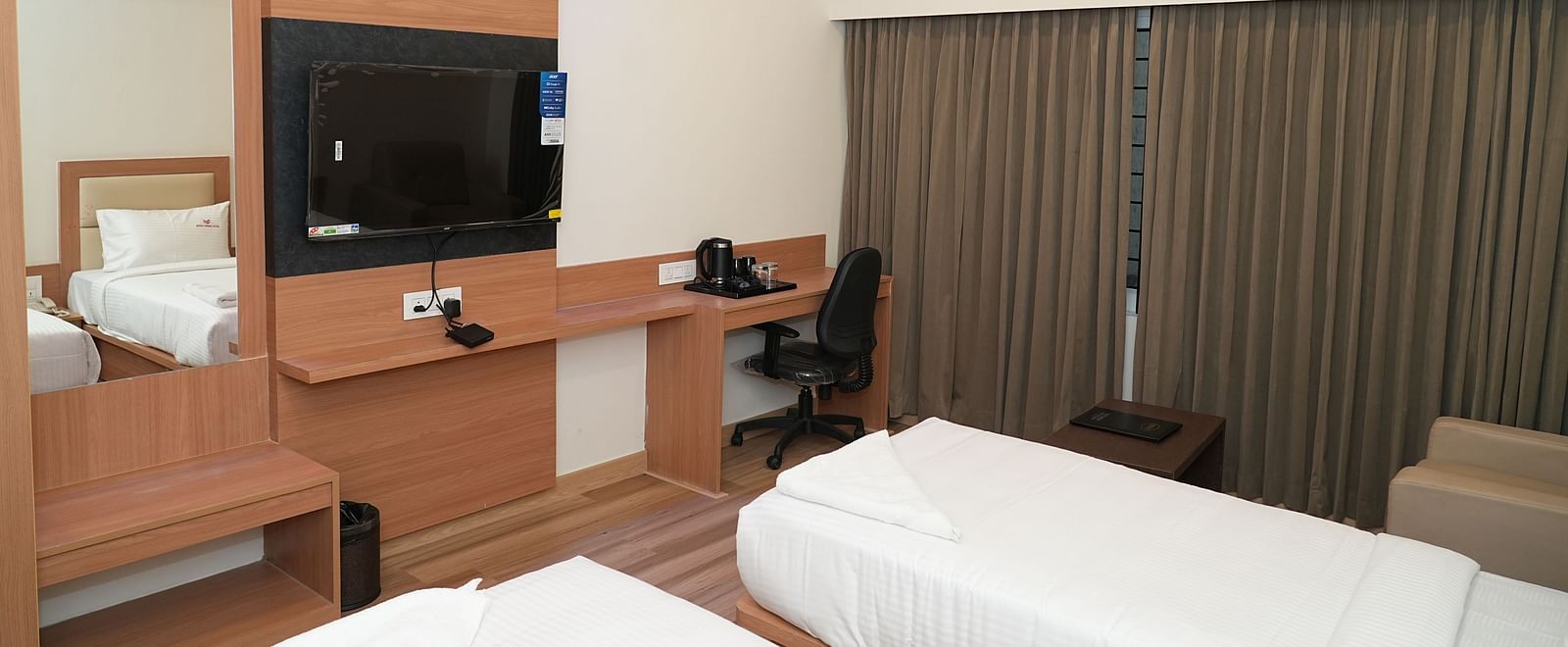 a bedroom with modern furnishings featuring a twin bed along with a medium mirror and a wall mounted television opposite to it - Hotel Grand Sigma