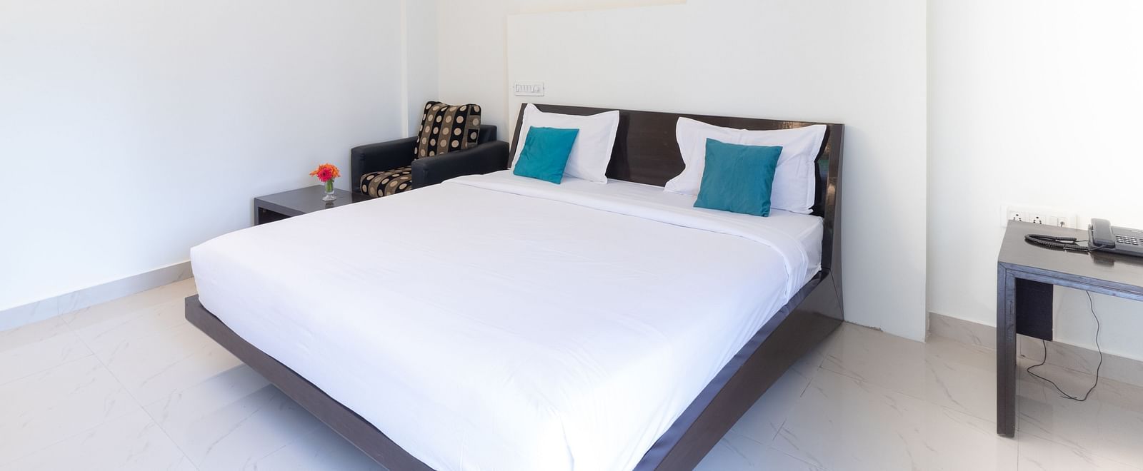 A well-lit room with a double bed with blue cushions and a simple bedside table at Sanctum Suites Domlur, Bangalore.