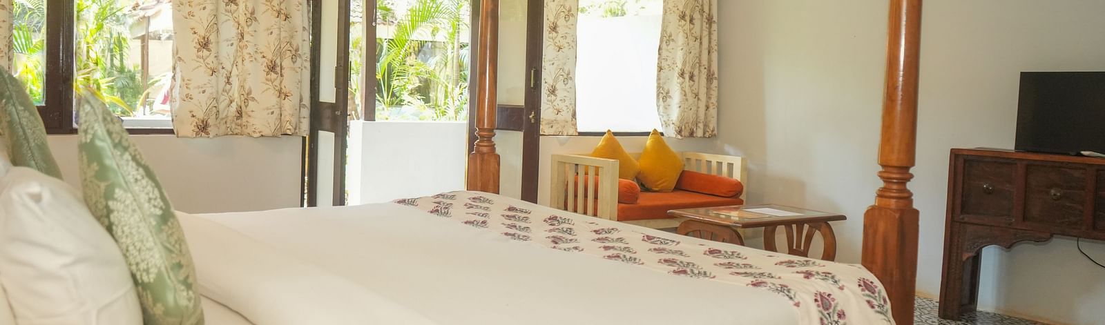 Side view of a canopy bed near large windows overlooking greenery at De Soul Santé, Morjim.