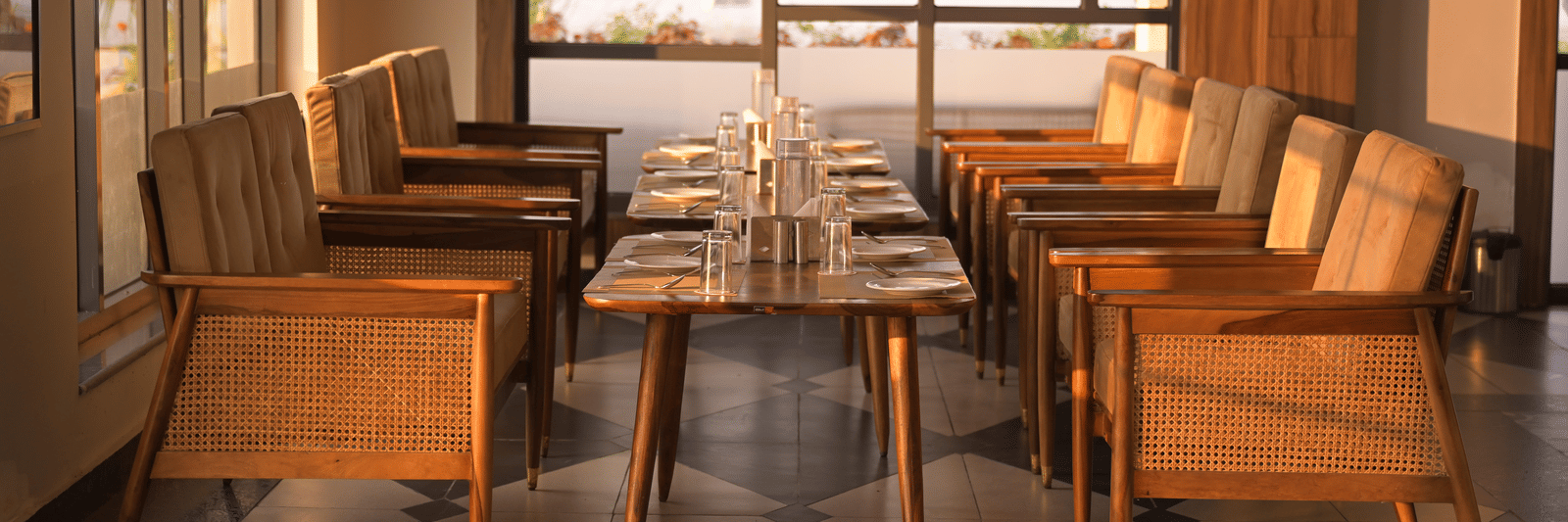 An elegant indoor seating area with wooden chairs and large windows framing outdoor garden views at Hotel Sonar Bangla Mayapur.