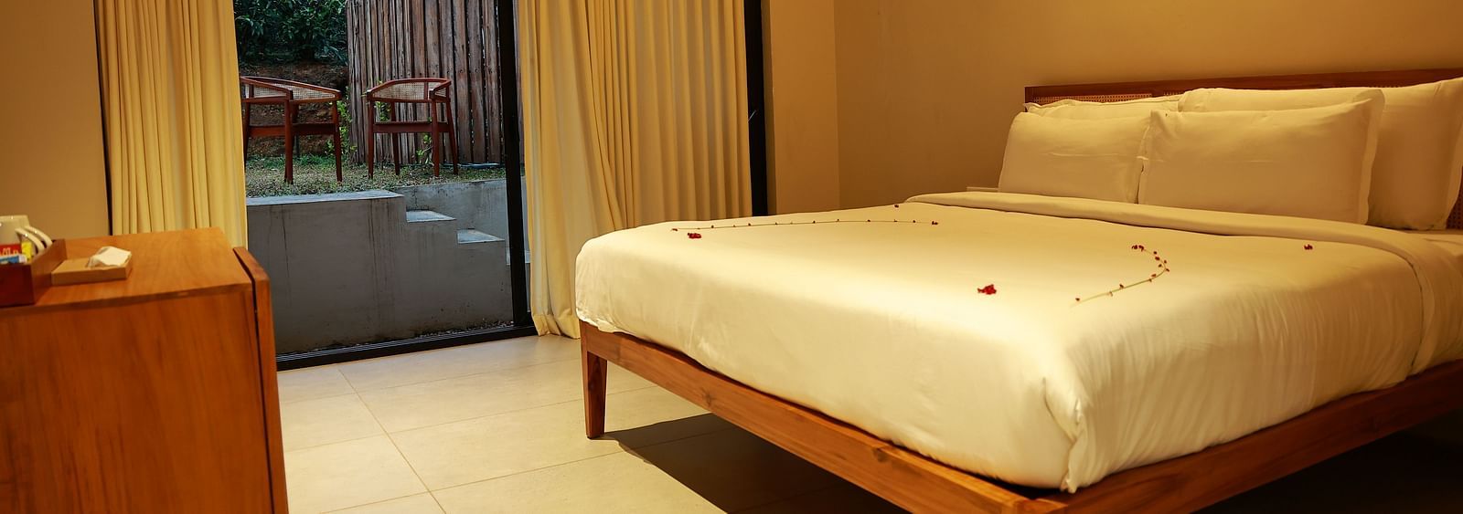  A hotel room at Vaasta Vagamon featuring a bed with subtle petal decor, a wooden cabinet, and a sliding door leading to an outdoor patio.