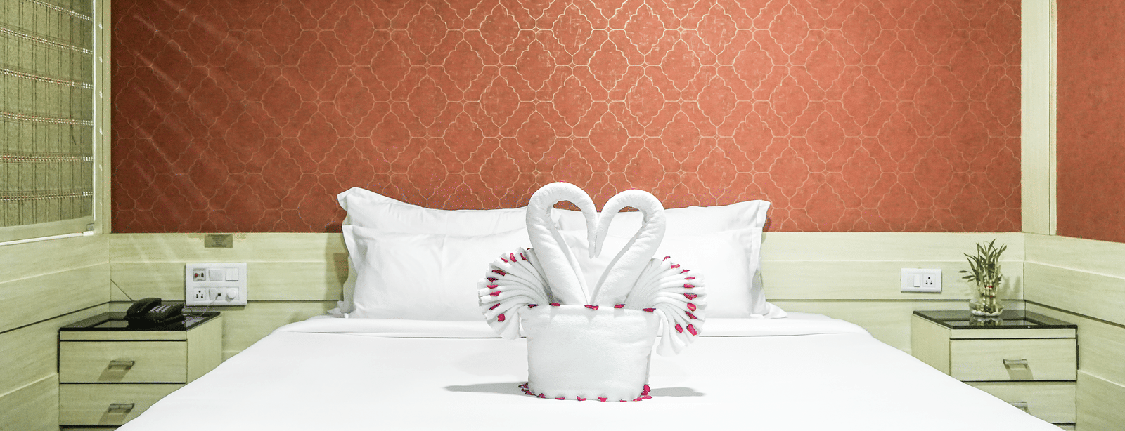 A room with a neatly made bed, featuring two swan-shaped towels at Infiniti Hotel, Indore.