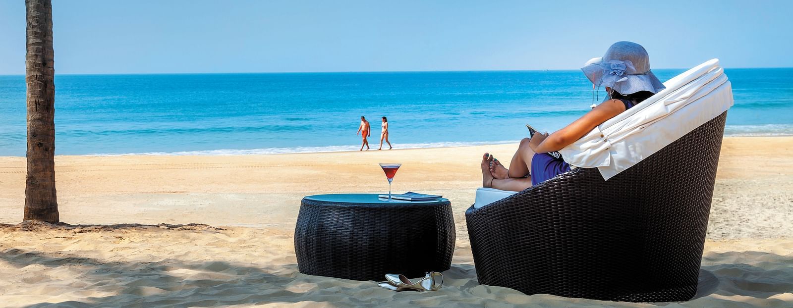 a woman sitting on the chair with a drink on the table on the beach - Caravela Beach Resort Goa.