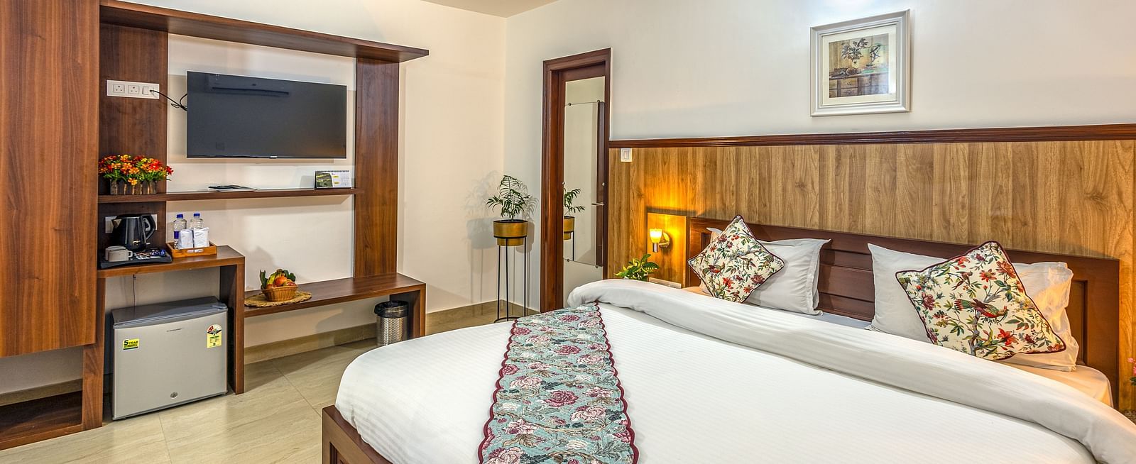 side view of a double bed with a tv wall mounted on the side inside one of the rooms - Neer Ganga Resorts