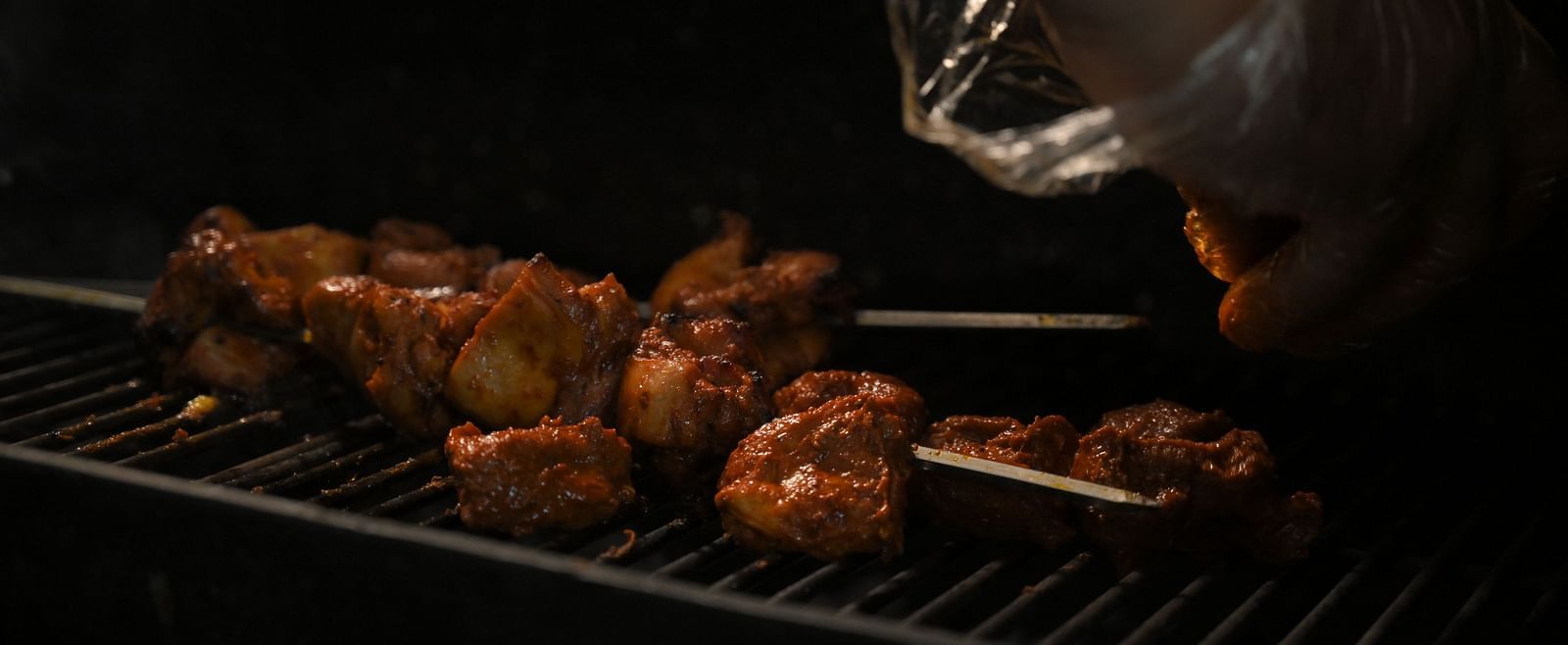 A chef carefully bastes grilled meat, showcasing culinary expertise at Royal Comfort Regency.