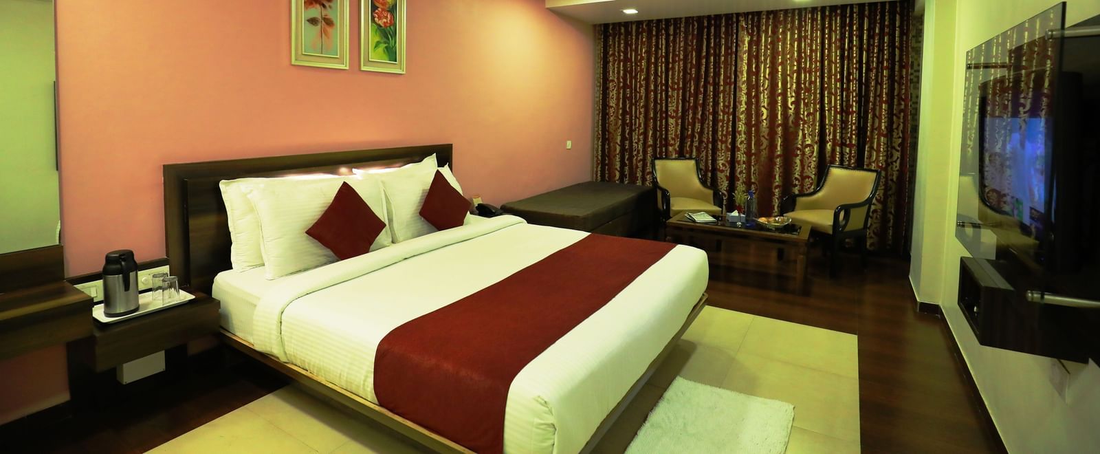 A bedroom at Krushnai Resort featuring a bed with a red runner, a flat-screen TV, and warm lighting.