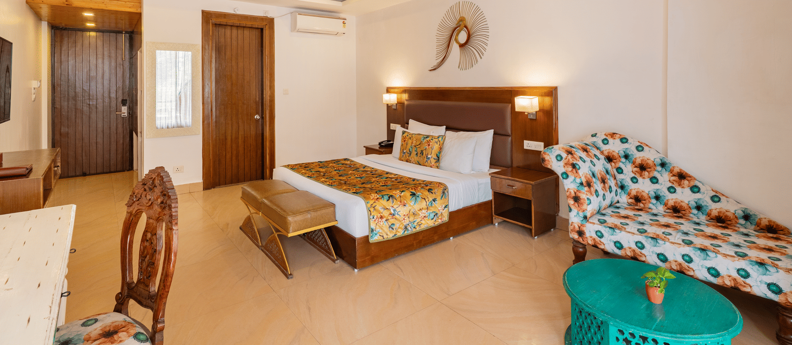 A bedroom featuring a neatly made bed, a bedside table, a sofa, a coffee table, a desk with a chair, and an art piece on the wall | Summit by the Ganges Beach Resort & Spa, Rishikesh