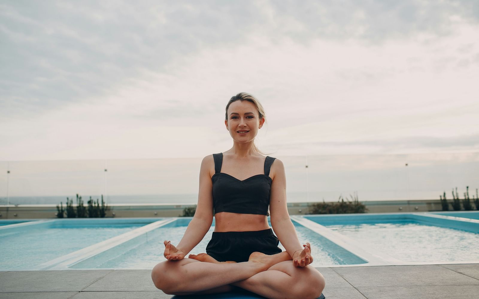 A woman posing for a picture while performing a pose in yoga next to the pool